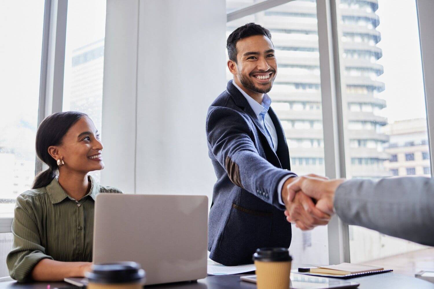 Smiling professionals shaking hands during successful office meeting negotiation