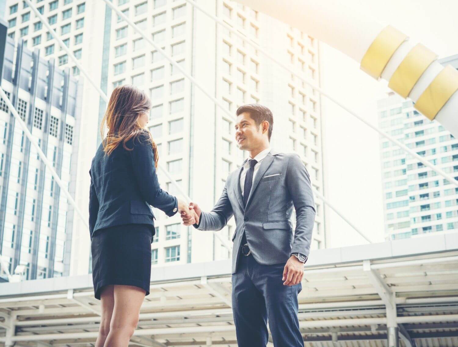 Successful business man and woman shaking hands front modern city skyscrapers