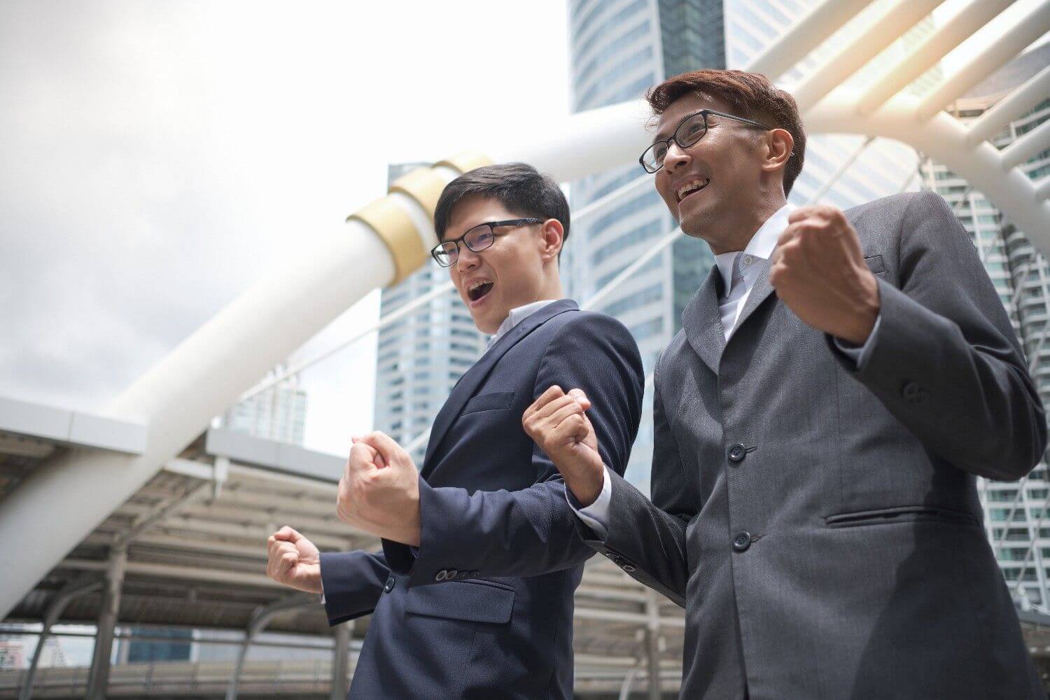 Two businessmen celebrating success with clenched fists cheering front city infrastructure