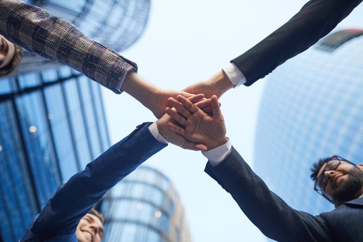 Unity diverse business team with hands stacked together against modern glass buildings