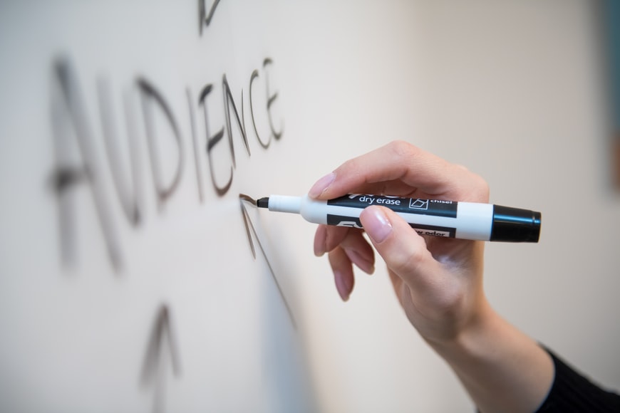 A person writing the word audience on a whiteboard