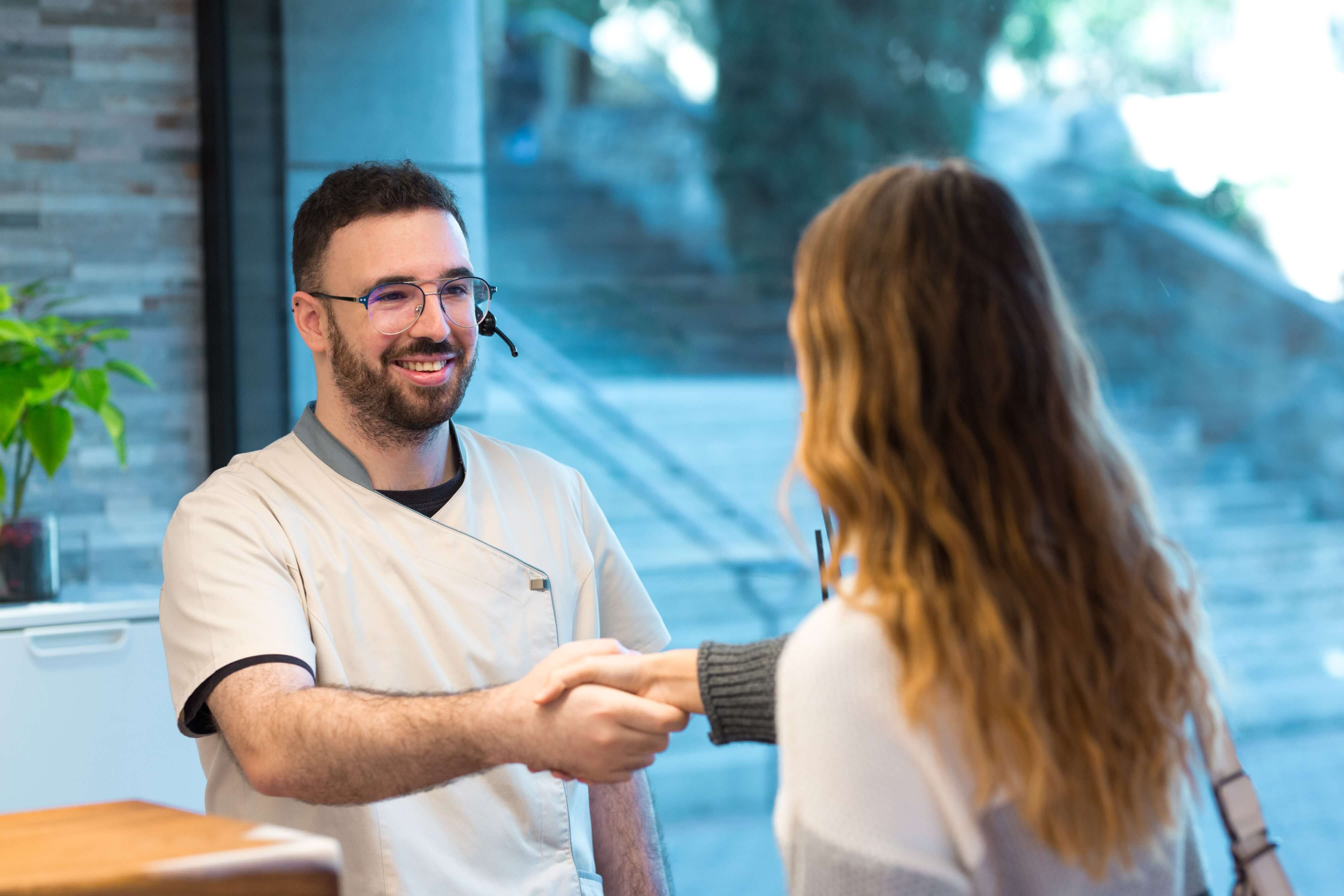 Smiling administrator shaking hand female patient reception desk